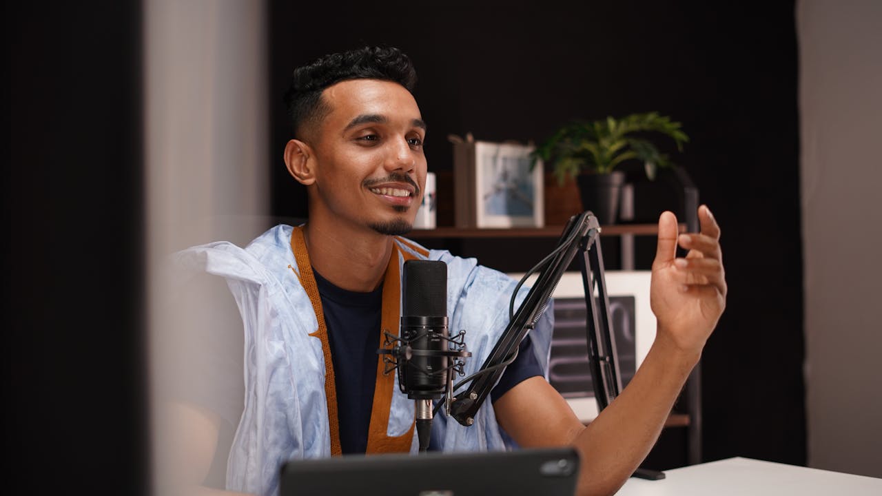 services-01 Smiling young man recording a podcast in a cozy home studio with professional microphone setup.