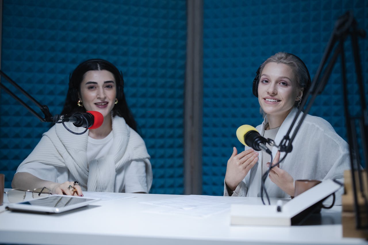 about-01 Two women podcasters engaging in discussion inside a modern recording studio with microphones.